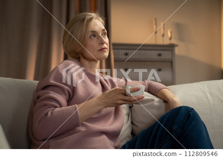 Woman Contemplating While Holding a Tea Cup in Her Living Room at Dusk 112809546