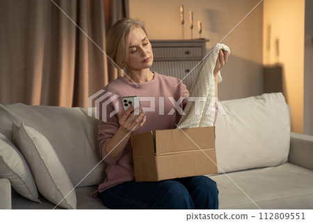 Woman Receives Package in Living Room While Using Smartphone at Evening Woman Receives Package in Living Room While Using Smartphone at Evening 112809551
