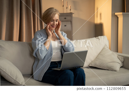 Woman Celebrates a Success While Using Laptop in a Cozy Living Room Setting Woman Celebrates a Success While Using Laptop in a Cozy Living Room Setting 112809655