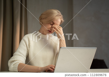 Woman Experiencing Stress or Fatigue While Working on Laptop Indoors 112809678