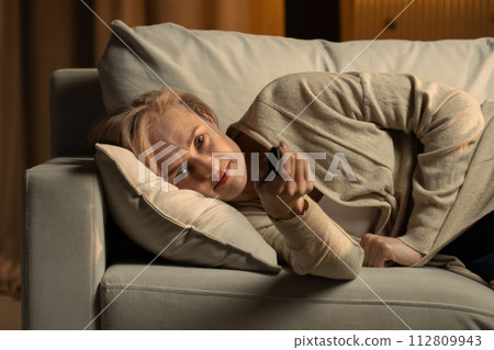 Mature Woman Relaxing on a Sofa While Watching Television at Home in the Evening 112809943