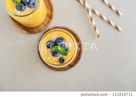 Refreshing and healthy mango smoothie with coconut flakes and fresh blueberries 112810711