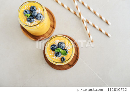Refreshing and healthy mango smoothie with coconut flakes and fresh blueberries 112810712