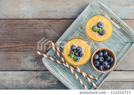 Refreshing and healthy mango smoothie in glasses with coconut flakes and fresh blueberries 112810715