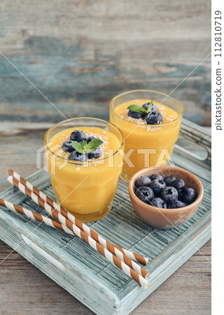 Refreshing and healthy mango smoothie in glasses with coconut flakes and fresh blueberries Refreshing and healthy mango smoothie in glasses with coconut flakes and fresh blueberries 112810719