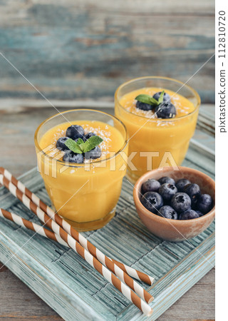 Refreshing and healthy mango smoothie in glasses with coconut flakes and fresh blueberries Refreshing and healthy mango smoothie in glasses with coconut flakes and fresh blueberries 112810720