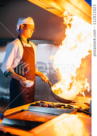Chef hands with wok and fire. Closeup of chef cooking food with flames in professional kitchen. Expertise at work busy cooking handling flames in a modern setting. cook food with fire Chef hands with wok and fire. Closeup of chef cooking food with flames in professional kitchen. Expertise at work busy cooking handling flames in a modern setting. cook food with fire 112811023