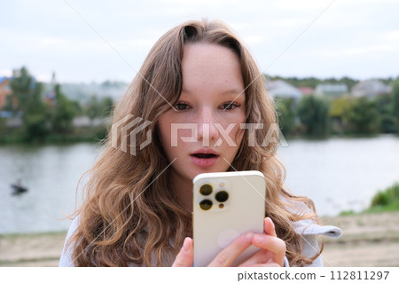 Young blonde woman using mobile phone with surprise facial expression. High quality photo 112811297