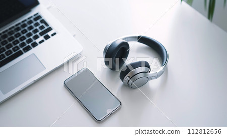 Modern tech gadgets, including sleek smartphone and stylish headphone, form a harmonious display on the spotless white surface Modern tech gadgets, including sleek smartphone and stylish headphone, form a harmonious display on the spotless white surface 112812656