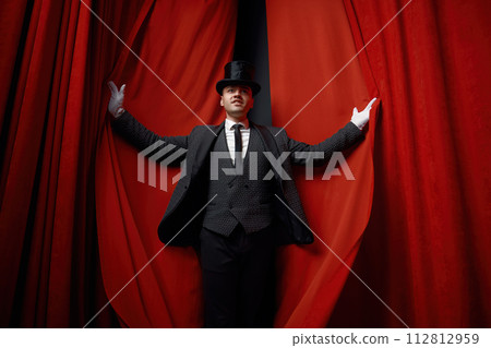 Cinematic posed portrait of magician actor over red velvet stage curtain 112812959