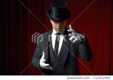 Waist-up portrait of handsome man magician showing mysterious trick on stage 112812960
