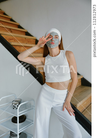 Happy young woman applying clay mask on face enjoying home beauty procedure Happy young woman applying clay mask on face enjoying home beauty procedure 112812973