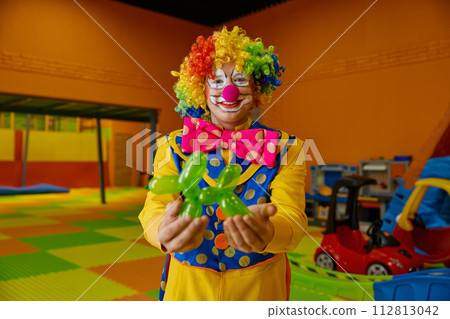 Funny clown holding balloon dog standing over playroom background 112813042