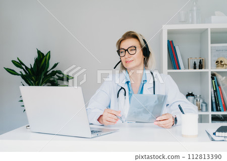 Female doctor in headset make online video call consult patient on laptop. Middle aged woman therapist videoconferencing for domestic health treatment. Telemedicine. Online remote medical appointment. 112813390