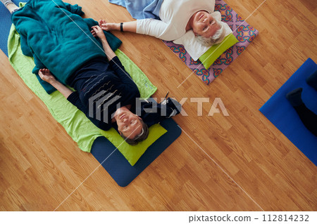 Top view of group of senior women engage in various yoga exercises, including neck, back, and leg stretches, under the guidance of a trainer in a sunlit space, promoting well-being and harmony Top view of group of senior women engage in various yoga exercises, including neck, back, and leg stretches, under the guidance of a trainer in a sunlit space, promoting well-being and harmony 112814232
