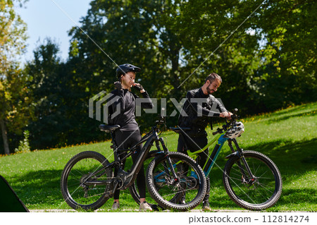 A sweet couple, equipped with bicycles and engrossed in coordinating their journey, checks their GPS mobile and watches while planning scenic routes in the park, seamlessly blending technology and A sweet couple, equipped with bicycles and engrossed in coordinating their journey, checks their GPS mobile and watches while planning scenic routes in the park, seamlessly blending technology and 112814274