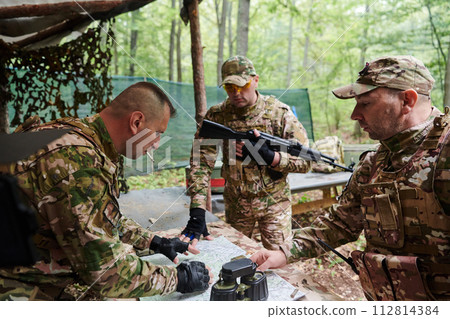A highly trained military unit strategizes and organizes a tactical mission while studying a military map during a briefing session A highly trained military unit strategizes and organizes a tactical mission while studying a military map during a briefing session 112814384