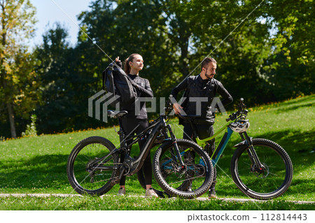 A sweet couple, equipped with bicycles and engrossed in coordinating their journey, checks their GPS mobile and watches while planning scenic routes in the park, seamlessly blending technology and A sweet couple, equipped with bicycles and engrossed in coordinating their journey, checks their GPS mobile and watches while planning scenic routes in the park, seamlessly blending technology and 112814443
