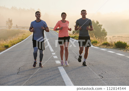 A group of friends, athletes, and joggers embrace the early morning hours as they run through the misty dawn, energized by the rising sun and surrounded by the tranquil beauty of nature 112814544