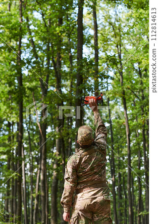 Elite military unit, equipped with state-of-the-art technology including a drone, strategically navigates and surveys dangerous wooded terrain, showcasing their precision, cooperation, and specialized 112814613