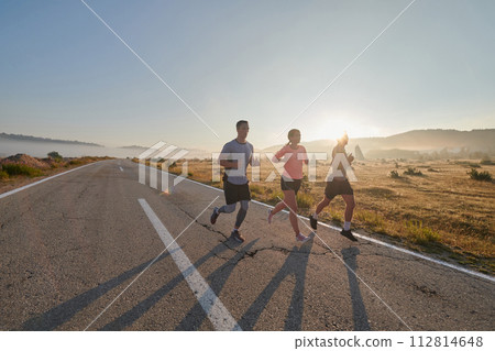 A group of friends, athletes, and joggers embrace the early morning hours as they run through the misty dawn, energized by the rising sun and surrounded by the tranquil beauty of nature A group of friends, athletes, and joggers embrace the early morning hours as they run through the misty dawn, energized by the rising sun and surrounded by the tranquil beauty of nature 112814648