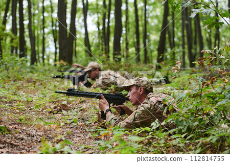 Elite soldiers stealthily maneuver through the dense forest, camouflaged in specialized gear, as they embark on a covert and strategic military mission 112814755