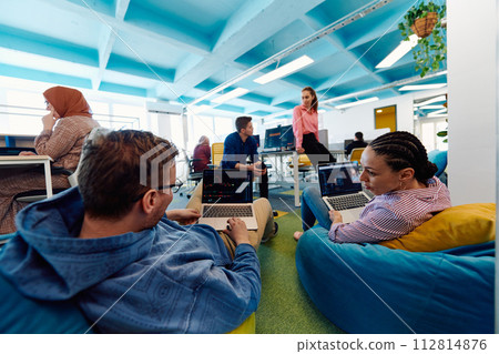 In a modern startup office, a diverse group of young and capable businesspeople engage in lively discussions about various projects, showcasing teamwork, innovation, and entrepreneurial spirit In a modern startup office, a diverse group of young and capable businesspeople engage in lively discussions about various projects, showcasing teamwork, innovation, and entrepreneurial spirit 112814876