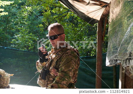 A military major employs a Motorola radio for seamless communication with his fellow soldiers during a tactical operation, showcasing professionalism and strategic coordination 112814921