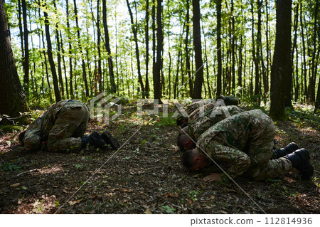 A dedicated group of soldiers engages in Islamic prayer amidst the challenging and perilous conditions of a military operation in dense forested areas 112814936