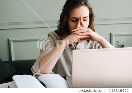 Stressed and Overworked Young Woman with Laptop, Battling Fatigue, Pressure, Migraine, and Stress 112816452