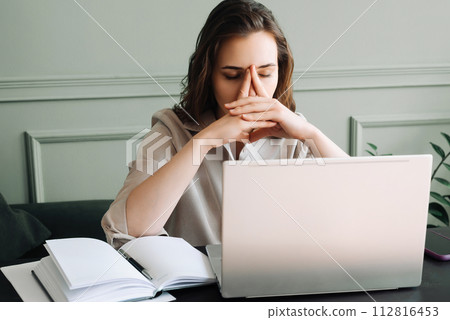 An unhappy tired woman with a laptop suffering from overwork, blood pressure, migraines and stress 112816453