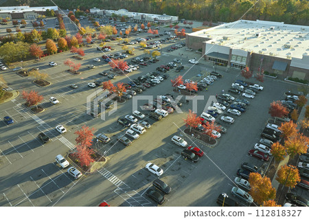 Aerial view grocery shopping mall and many colorful cars parked on parking lot with lines and markings for parking places and directions. Place for vehicles in front of a strip mall plaza Aerial view grocery shopping mall and many colorful cars parked on parking lot with lines and markings for parking places and directions. Place for vehicles in front of a strip mall plaza 112818327