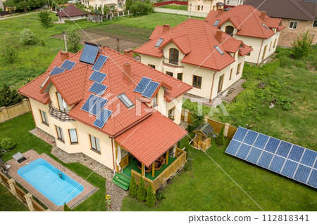Aerial view of a new autonomous house with solar panels and water heating radiators on the roof and green yard with blue swimming pool 112818341