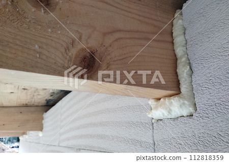 Installation of wooden beams of roof frame with spray foam on a house wall under construction. 112818359