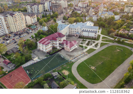 Aerial view of a football field on a stadium covered with green grass and a school building in city area. 112818362