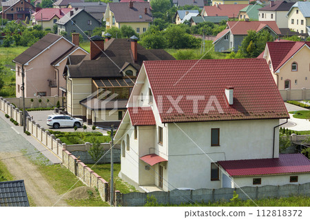 Quiet residential area with new expensive two- story cottages with brick fence and tile roofs and white sport car parked in front of garage door in paved well-kept yard. Luxury and prosperity concept. 112818372