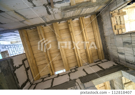 Close-up detail of house room interior under construction and renovation. Energy saving walls of hollow foam insulation blocks, wooden ceiling beams for roof frame. Close-up detail of house room interior under construction and renovation. Energy saving walls of hollow foam insulation blocks, wooden ceiling beams for roof frame. 112818407