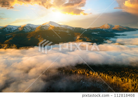 Aerial view of vibrant sunrise over Carpathian mountain hills covered with evergreen spruce forest in autumn. 112818408