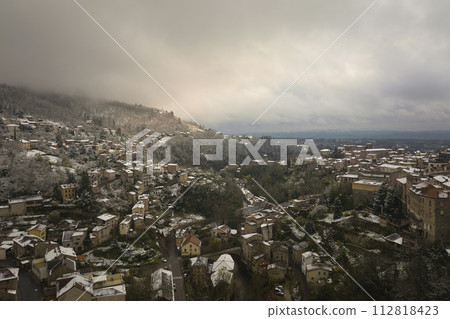 Aerial winter landscape of dense historic center of Thiers town in Puy-de-Dome department, Auvergne-Rhone-Alpes region in France. Rooftops of old buildings and narrow streets at snowfall 112818423