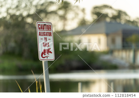 Alligator danger warning signpost in Florida waterfront park about caution and safety during walking near water 112818454