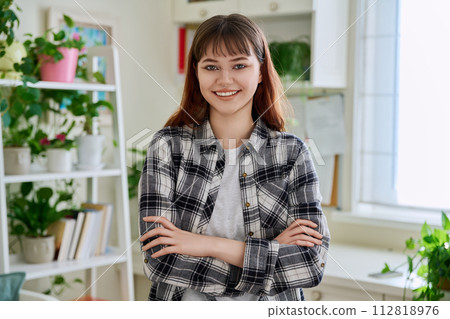 Portrait of smiling female teenager looking at camera with crossed arms in home 112818976