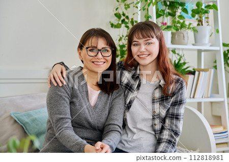 Portrait of happy hugging mother and teenage daughter sitting together on couch Portrait of happy hugging mother and teenage daughter sitting together on couch 112818981