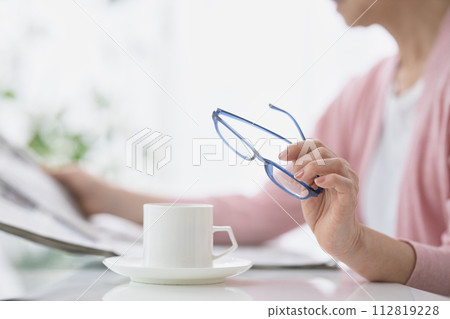 Hand of a middle-aged woman reading a newspaper with reading glasses in hand 112819228
