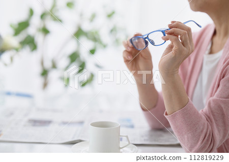 Hand of a middle-aged woman reading a newspaper with reading glasses in hand 112819229