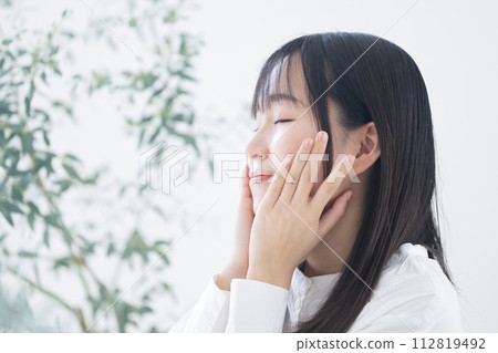 一位年輕的亞洲（日本）女性透過雙手觸摸臉頰和皮膚來關心皮膚護理的美容形象 112819492