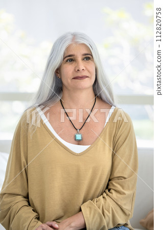 Thoughtful senior Hispanic woman sitting on home couch 112820758