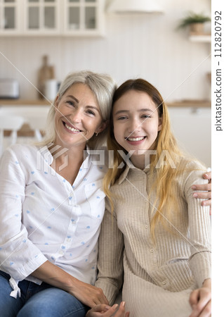 Middle-aged mother cuddling pretty pre-teen daughter, looking at camera 112820792
