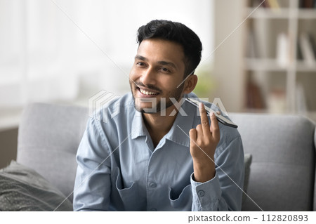 Smiling young Indian man listening pleasant audio message Smiling young Indian man listening pleasant audio message 112820893