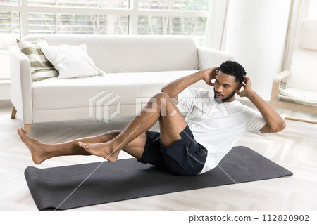 Focused young African athlete guy twisting body in boat pose 112820902