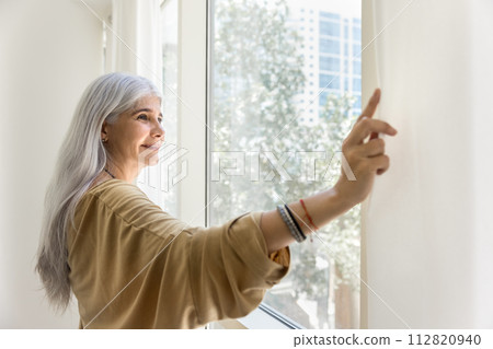 Positive relaxed elder Hispanic lady parting white transparent curtains Positive relaxed elder Hispanic lady parting white transparent curtains 112820940
